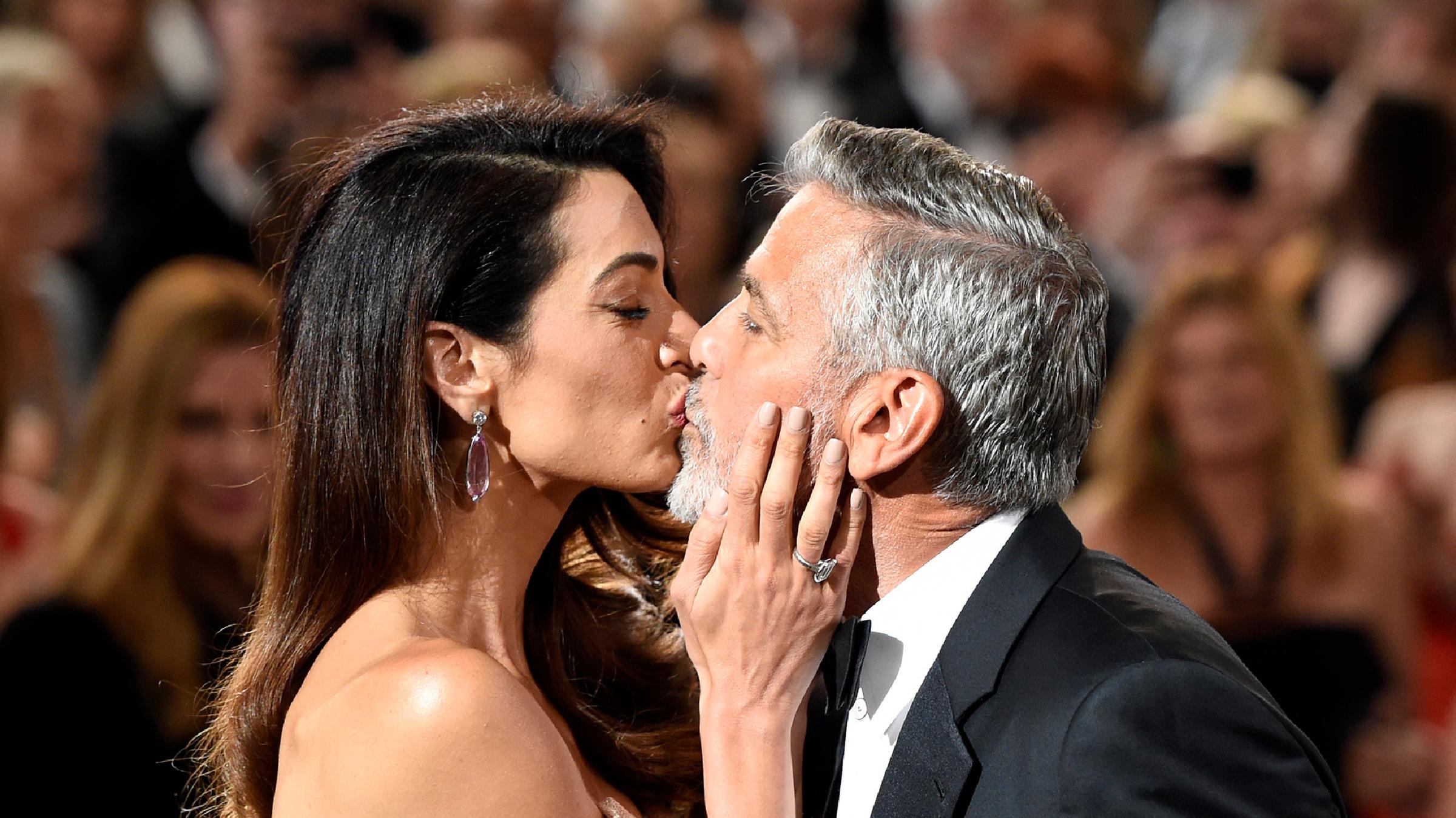 George und Amal Clooney küssen sich.
