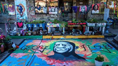 Ein auf den Bürgersteig gemaltes Porträt von George Floyd steht im Mittelpunkt einer Gedenkstätte, umgeben von Blumen, Kunstwerken und Ehrungen vor einem Ladengeschäft am George Floyd Square in Minneapolis, Minnesota, am 22. Mai 2025. 