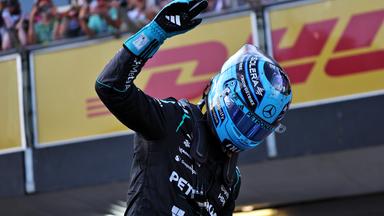 Rennfahrer in schwarzem Overall und blauem Helm grüsst die Fans