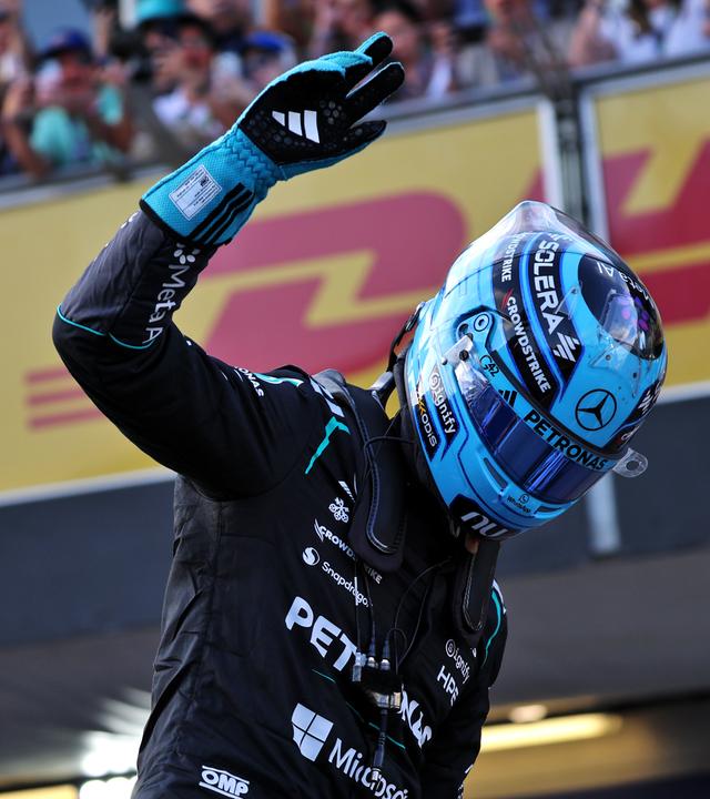 Rennfahrer in schwarzem Overall und blauem Helm grüsst die Fans