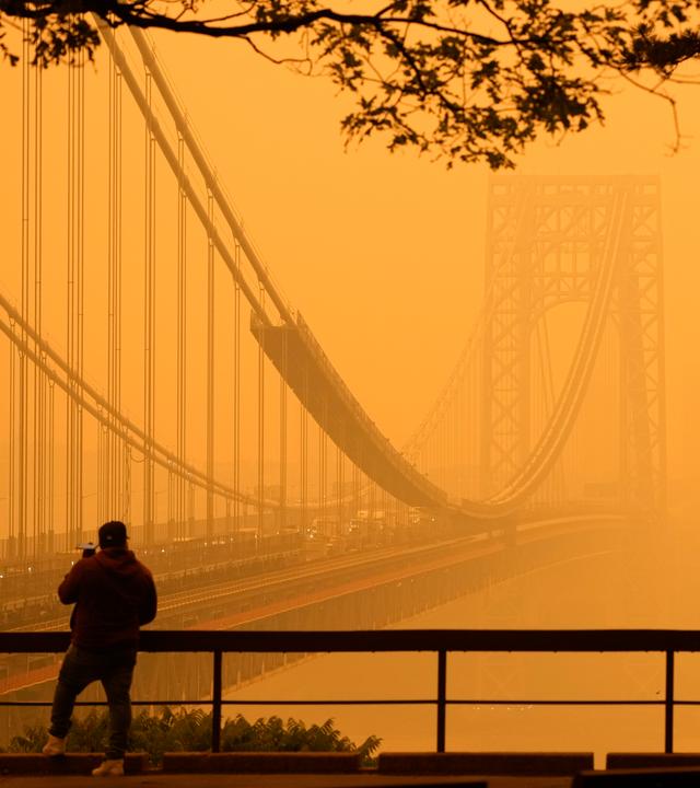 Ein Mann telefoniert, während er durch den Dunst vor der George Washington Bridge sieht.