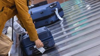Frau steht am Gepäckband eines Flughafens und greift nach einem Koffer.