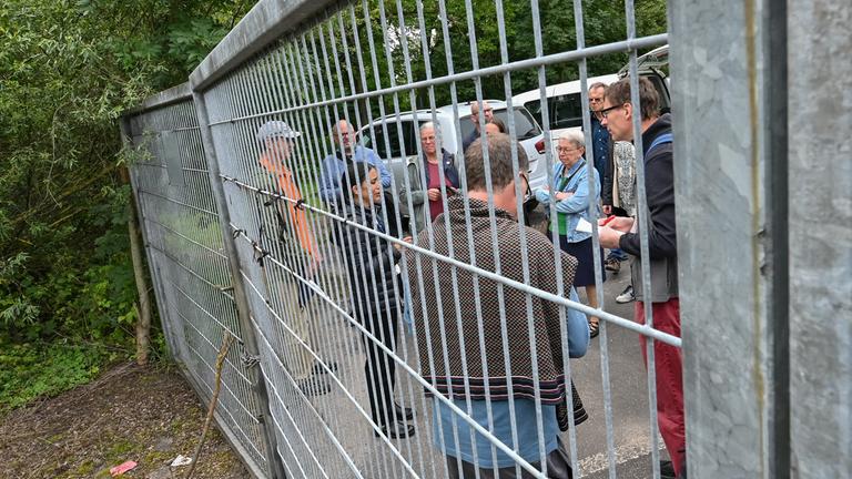 Diana Gonzalez Olivo, Landesintegrationsbeauftragte Brandenburg und Wolfgang Henschel, künftiger Ortsvorsteher von Küstrin-Kietz, stehen vor einem verschlossenem Tor zu einem Gelände mit alten Kasernenanlagen.