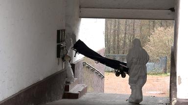 Beamte der Spurensicherung mit weißen Anzügen bringen einen Trage in ein Wohnhaus.
