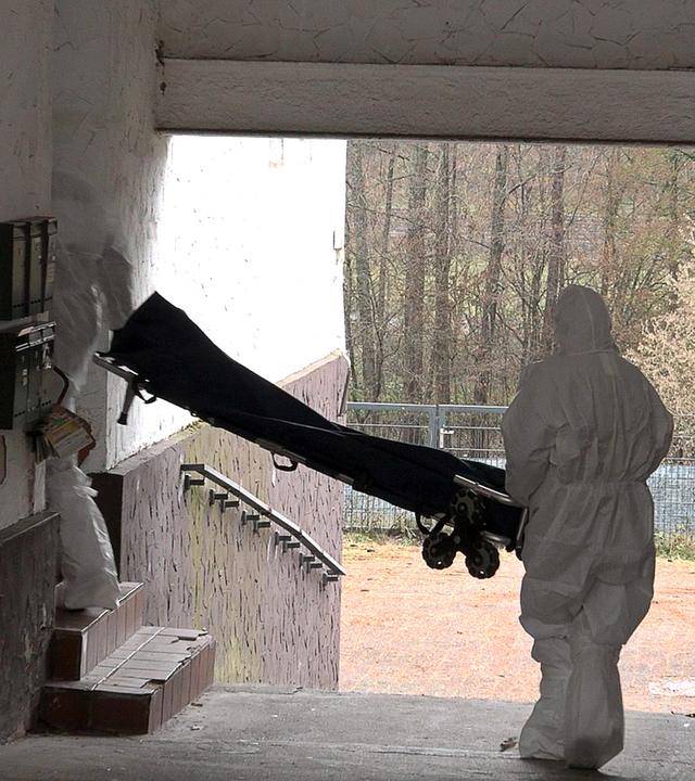 Beamte der Spurensicherung mit weißen Anzügen bringen einen Trage in ein Wohnhaus.