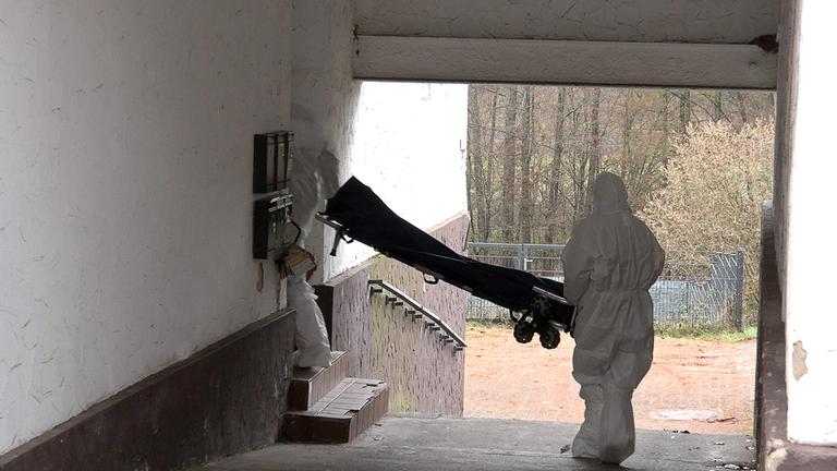 Beamte der Spurensicherung mit weißen Anzügen bringen einen Trage in ein Wohnhaus.