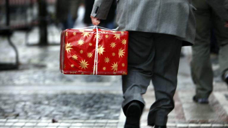 Ein Mann in grauem Anzug trägt ein großes, rotes Paket durch die Innenstadt.