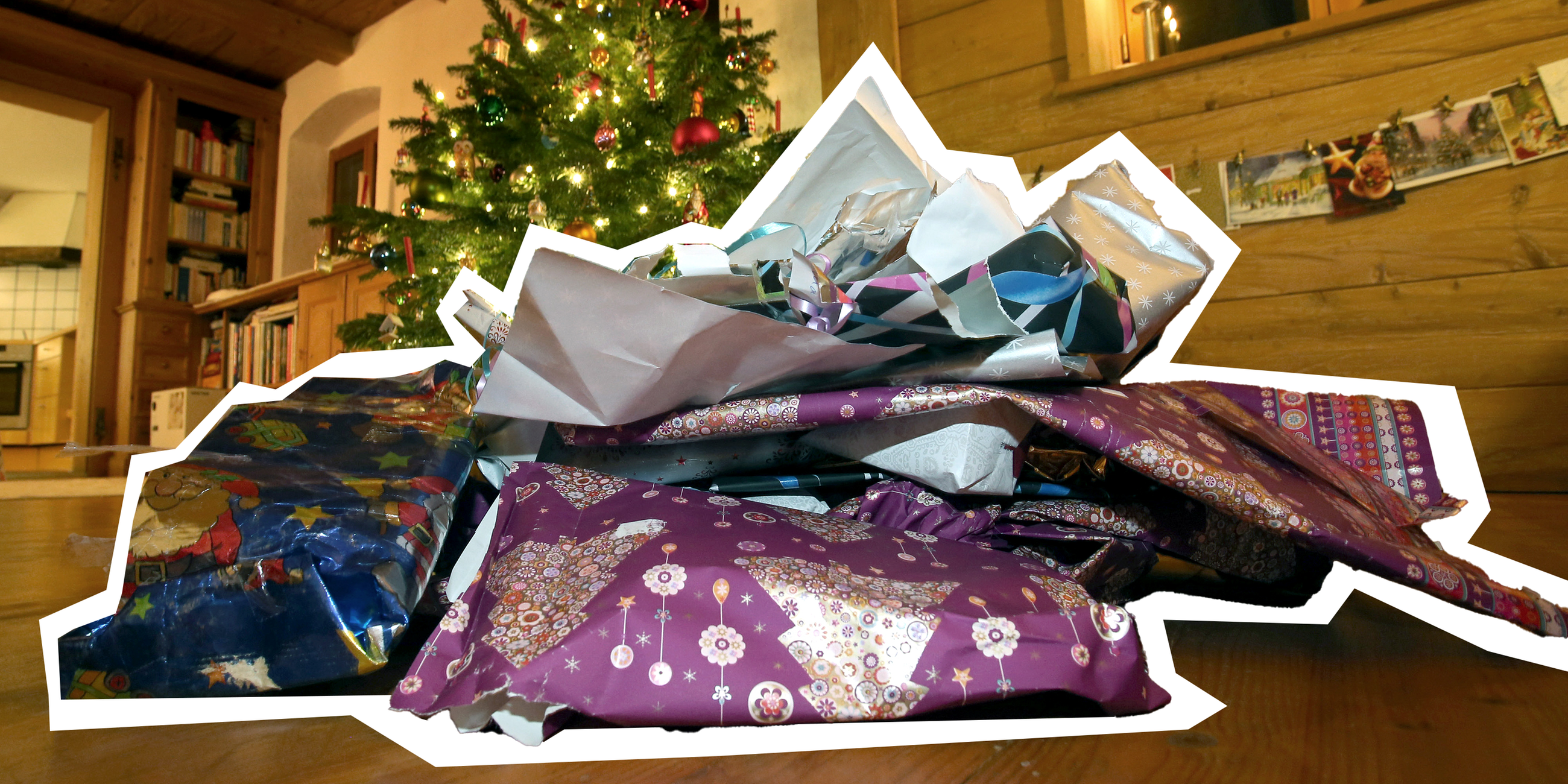 Zerknülltes weihnachtliches Geschenkpapier liegt vor einem geschmücktem Christbaum