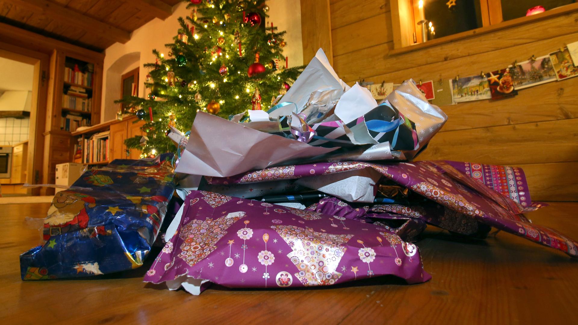 Zerknülltes weihnachtliches Geschenkpapier liegt vor einem geschmücktem Christbaum.