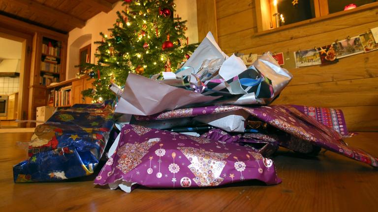 Zerknülltes weihnachtliches Geschenkpapier liegt vor einem geschmücktem Christbaum.