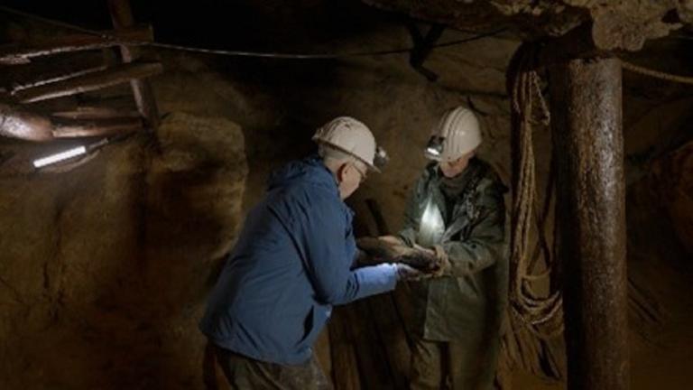 Zwei Männer mit Schutzhelmen stehen in einem dunklen Stollen.