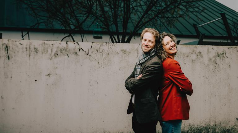 Anna und Sebastian stehen Rücken an Rücken.