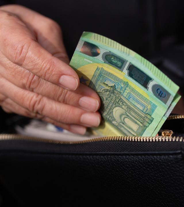 Seniorin steckt Euroscheine in eine Geldbörse 