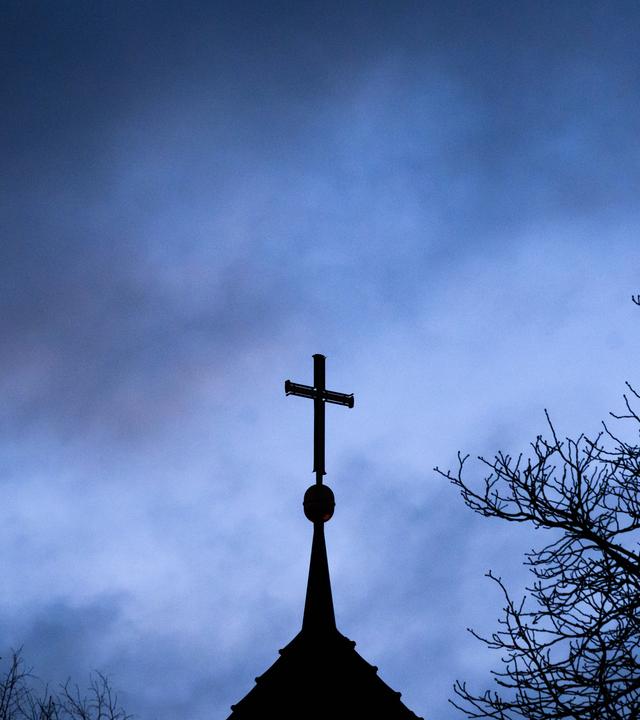 Dunkle Wolken ziehen über das Kreuz auf einer evangelischen Kirche in der Region Hannover hinweg.