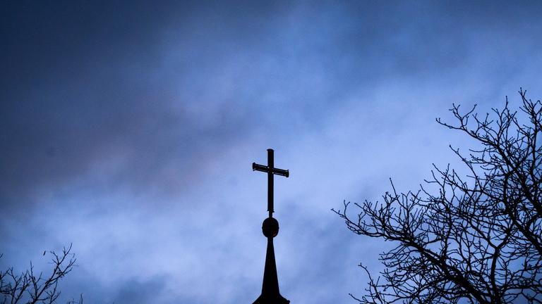 Dunkle Wolken ziehen über das Kreuz auf einer evangelischen Kirche in der Region Hannover hinweg.