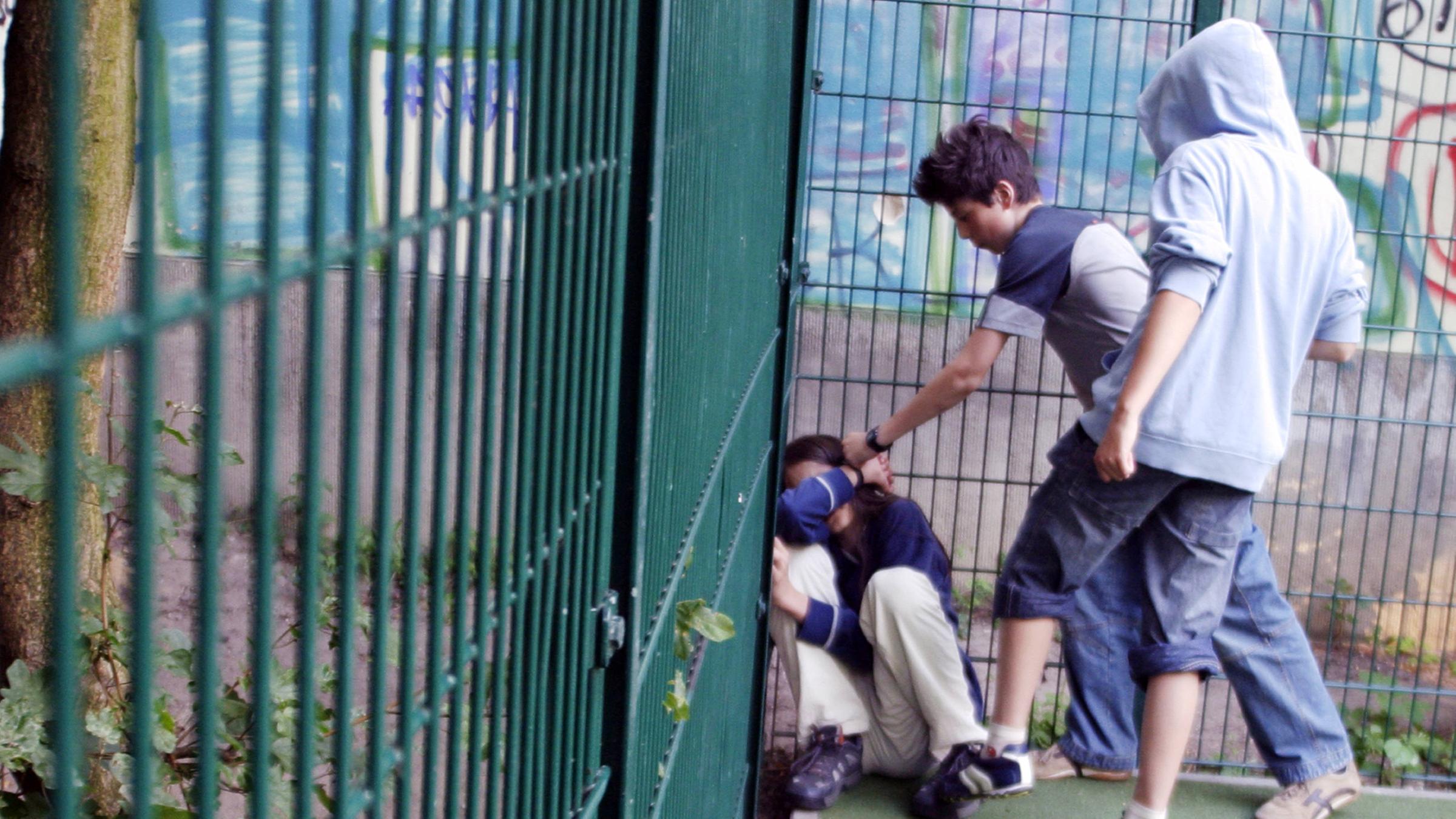 Zwei Jungs prügeln sich auf einem Sportplatz einen anderen Jungen.