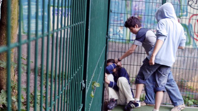 Zwei Jungs prügeln sich auf einem Sportplatz einen anderen Jungen.