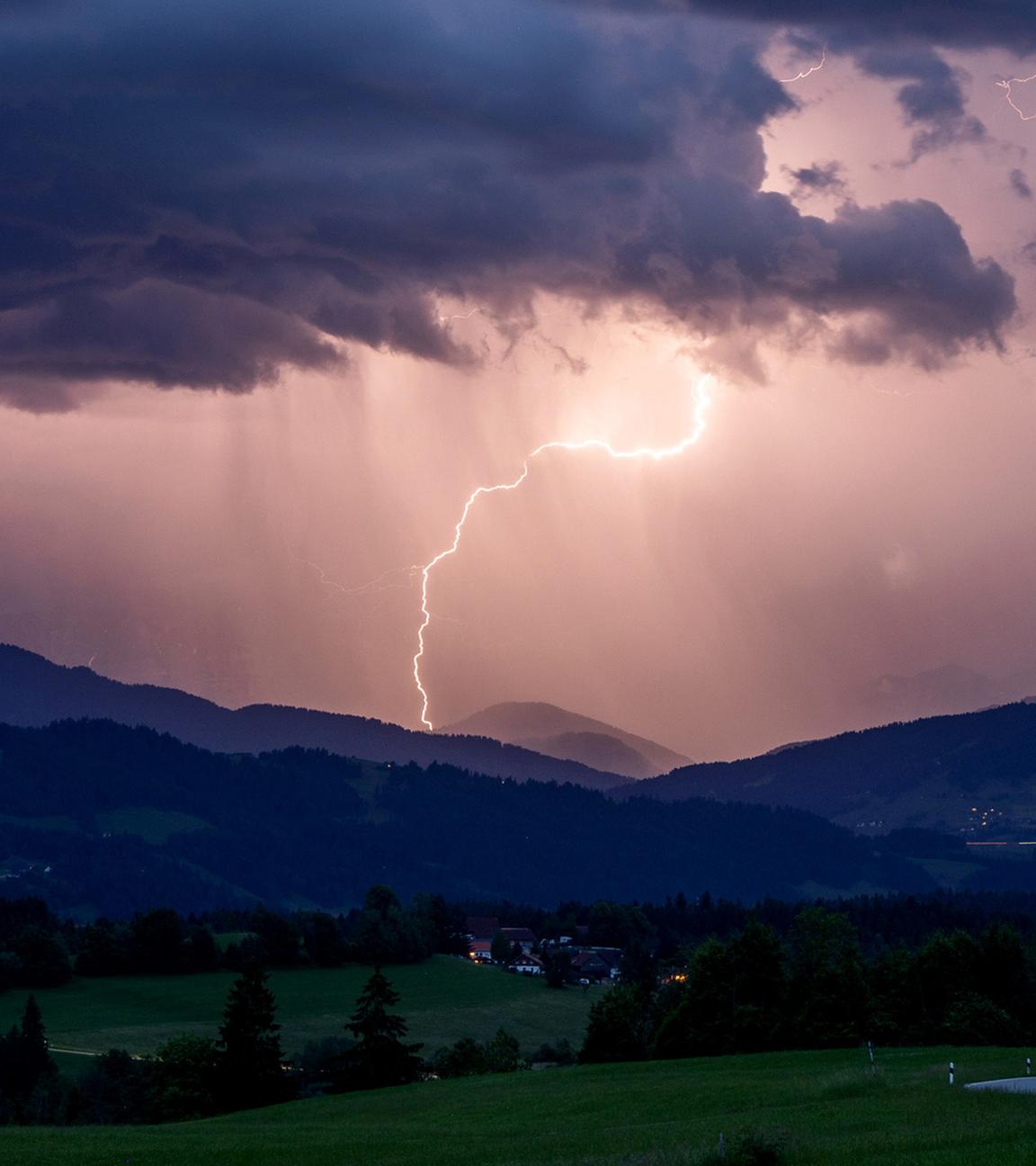 Blitze entladen sich über den Alpen während eines aufziehenden Gewitters am Abend hinter der St. Hubertus Kapelle in Scheidegg am 01.06.2025.