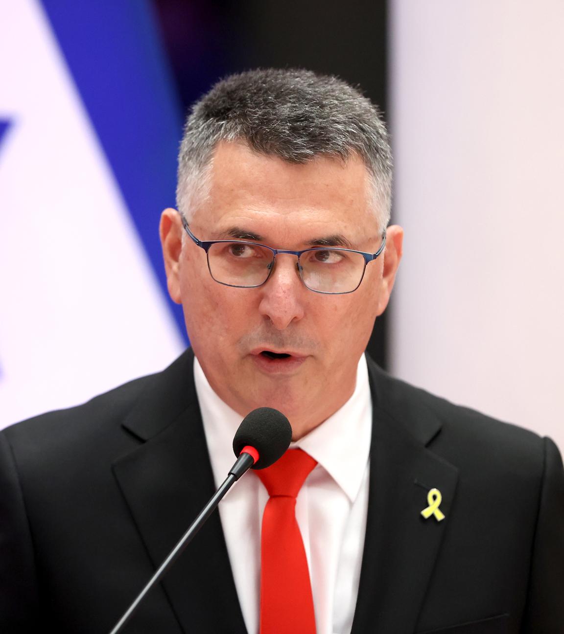 Gideon Saar spricht in ein Mikrofon vor einer israelischen Flagge