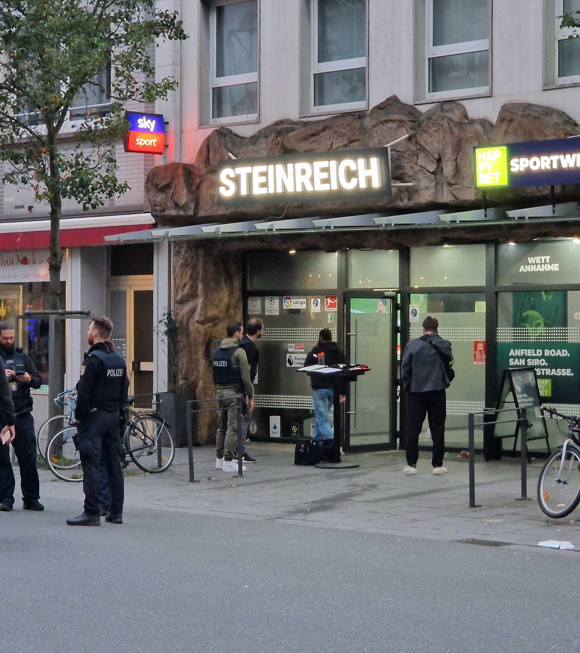Polizisten und weitere Personen stehen vor einem Sportwettbüro.