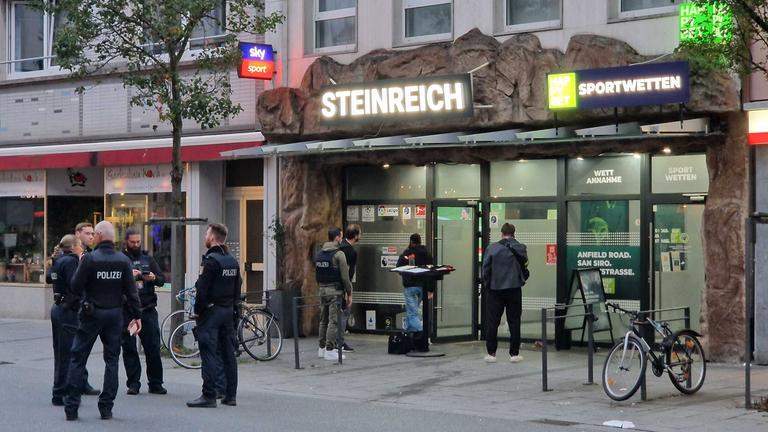 Polizisten und weitere Personen stehen vor einem Sportwettbüro.