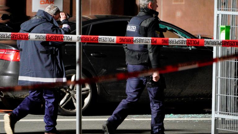 Hessen, Gießen: Zwei Einsatzkräfte der Polizei laufen an dem Unfallfahrzeug, mit einer zerbrochenen Beifahrerscheibe, entlang.