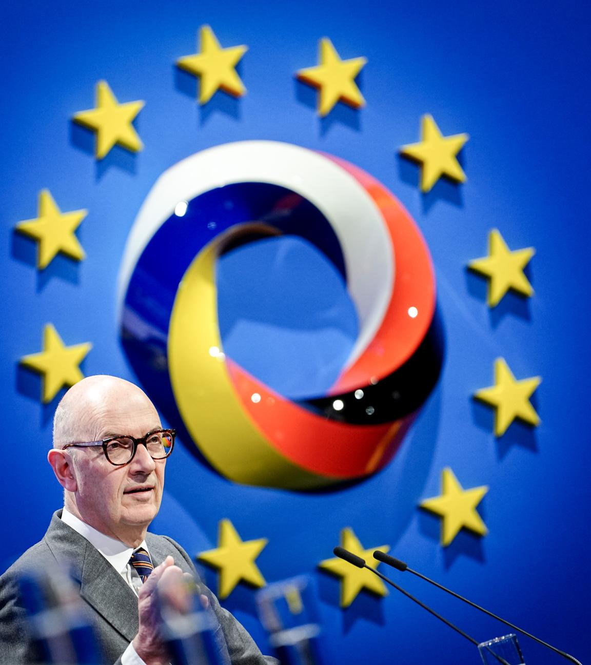 Auf dem Bild ist das Logo der Konferenz zu sehen. Davor steht ein Mann auf der Bühne und spricht ins Mikrofon.