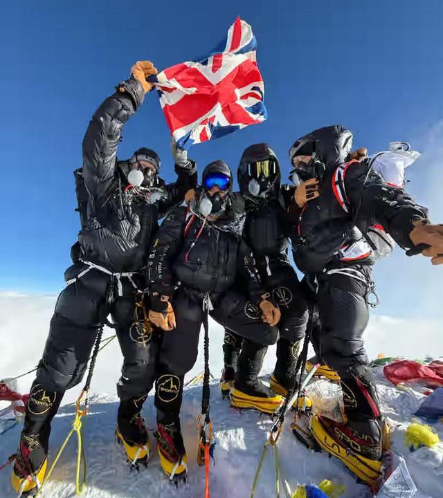 Vier schwarz gekleidete Menschen auf dem Gipfel des Mount Everest