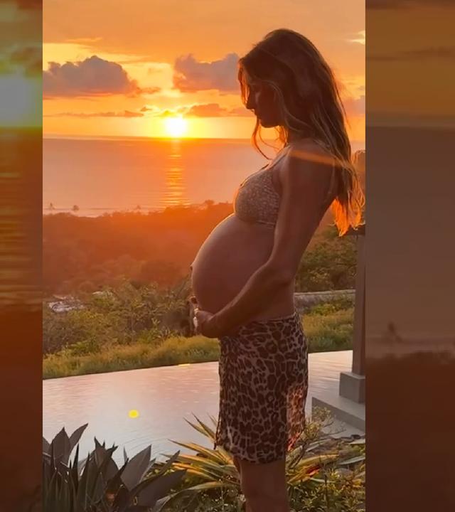 Die schwangere Gisele Bündchen steht vor einem Sonnenuntergang.