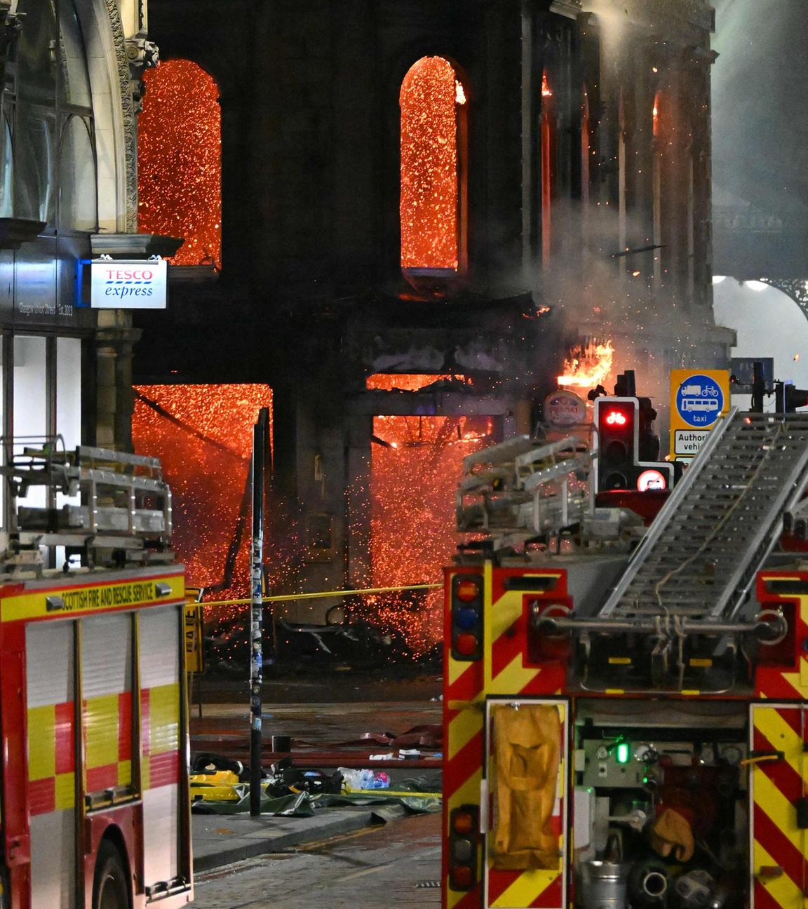 Gebäude steht nachts unter Flammen, davor parken Feuerwehrautos.