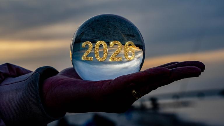 Êine Hand hält in der Dämmerung eine Glaskugel, auf der 2026 in Gold steht.