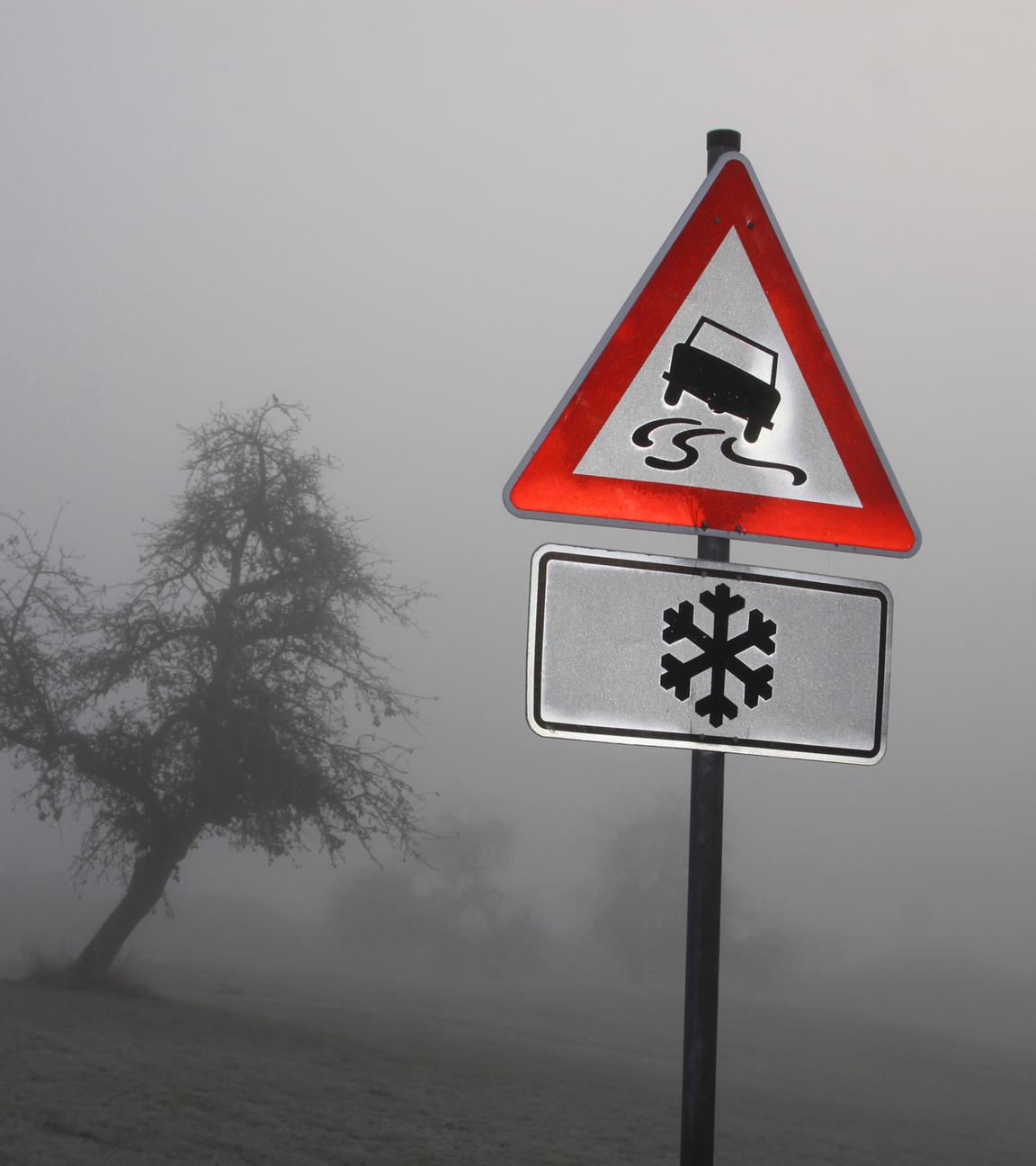 Ein Verkehrsschild im Nebel warnt vor Schleudergefahr