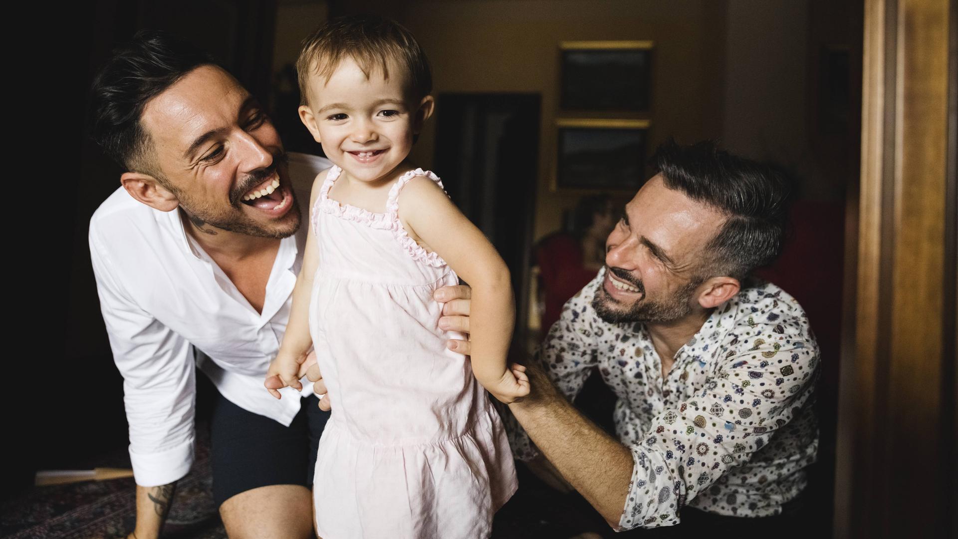 Glückliches schwules Paar spielt mit ihrer kleinen Tochter zu Hause