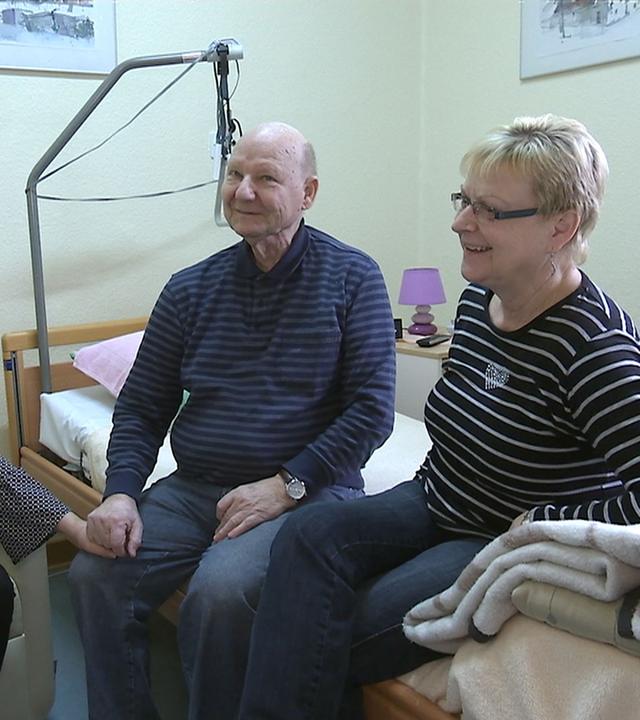 Drei Personen sitzen auf einem Krankenbett.