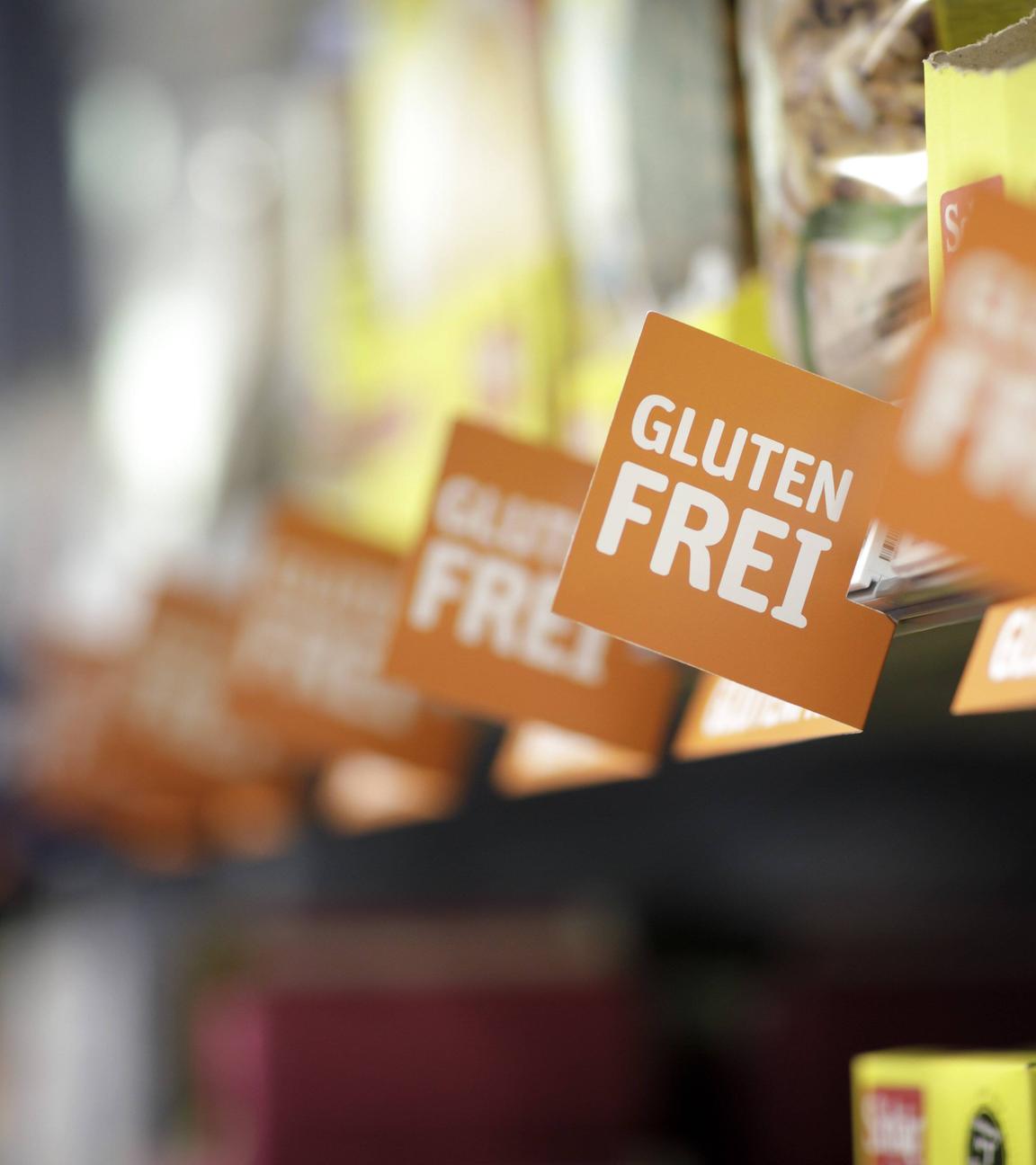 Ein Supermarktregal mit unkenntlich gemachten Produkten und Schildern mit der Aufschrift glutenfrei davor.