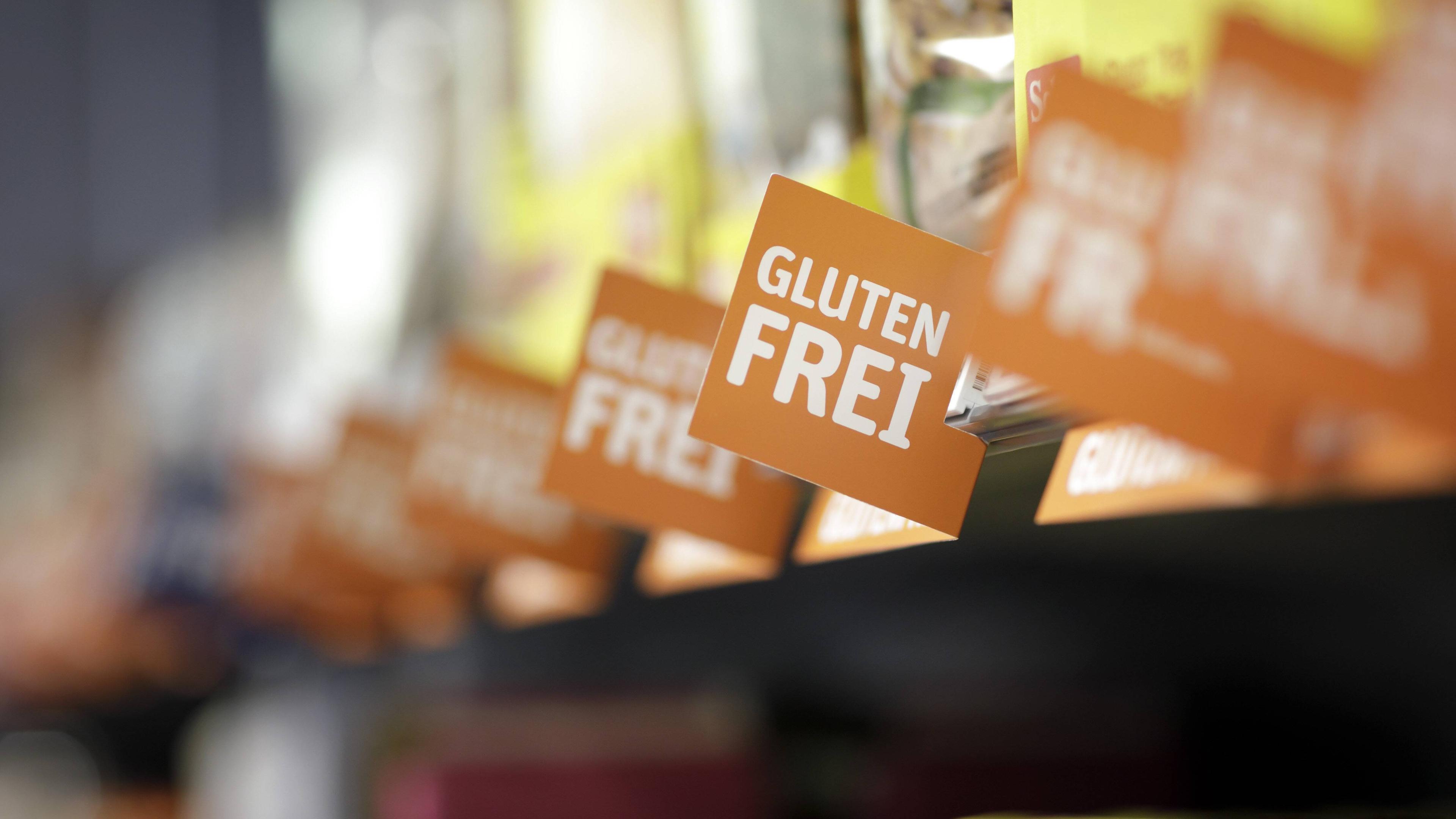 Ein Supermarktregal mit unkenntlich gemachten Produkten und Schildern mit der Aufschrift glutenfrei davor.