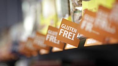 Ein Supermarktregal mit unkenntlich gemachten Produkten und Schildern mit der Aufschrift glutenfrei davor.