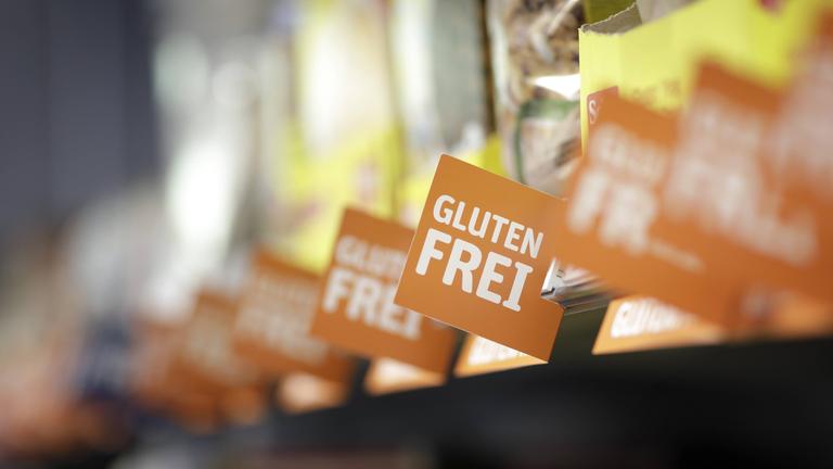 Ein Supermarktregal mit unkenntlich gemachten Produkten und Schildern mit der Aufschrift glutenfrei davor.