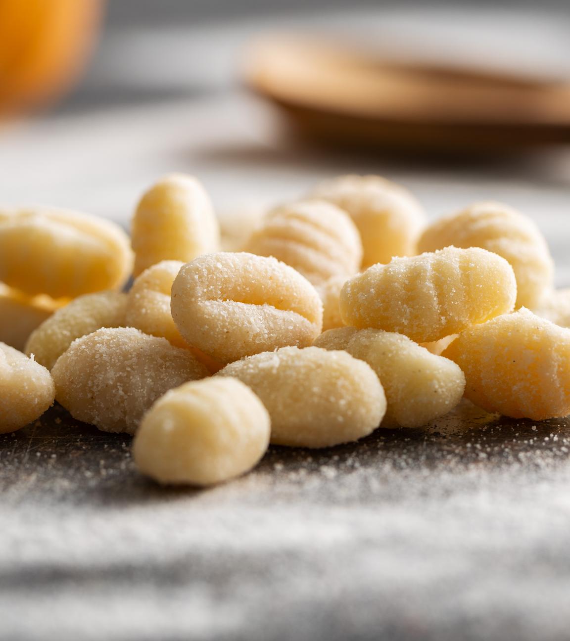 Eine handvoll ungekochter Gnocchi liegt auf einer dunklen, mit Mehl bestäubten Oberfläche in der Küche.