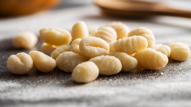 Eine handvoll ungekochter Gnocchi liegt auf einer dunklen, mit Mehl bestäubten Oberfläche in der Küche.