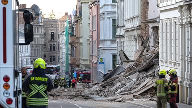 Einsatzkräfte von Polizei und Feuerweht stehen in der Nähe eines eingestürzten Hauses in der Innenstadt von Görlitz