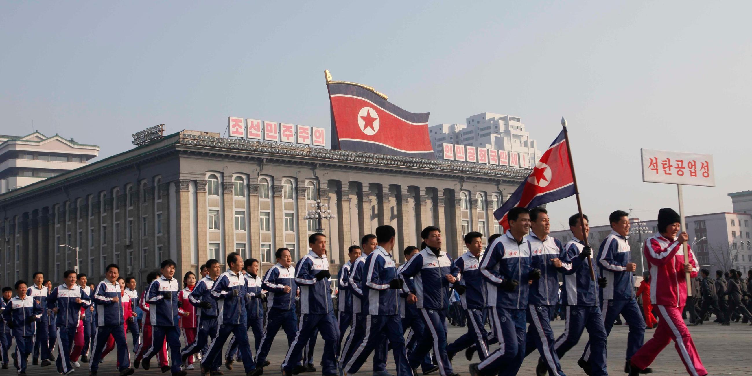 Eine Gruppe nordkoreanischer Regierungsbeamter joggt in Pjoengjang über den Kim-Il-Sung-Platz.