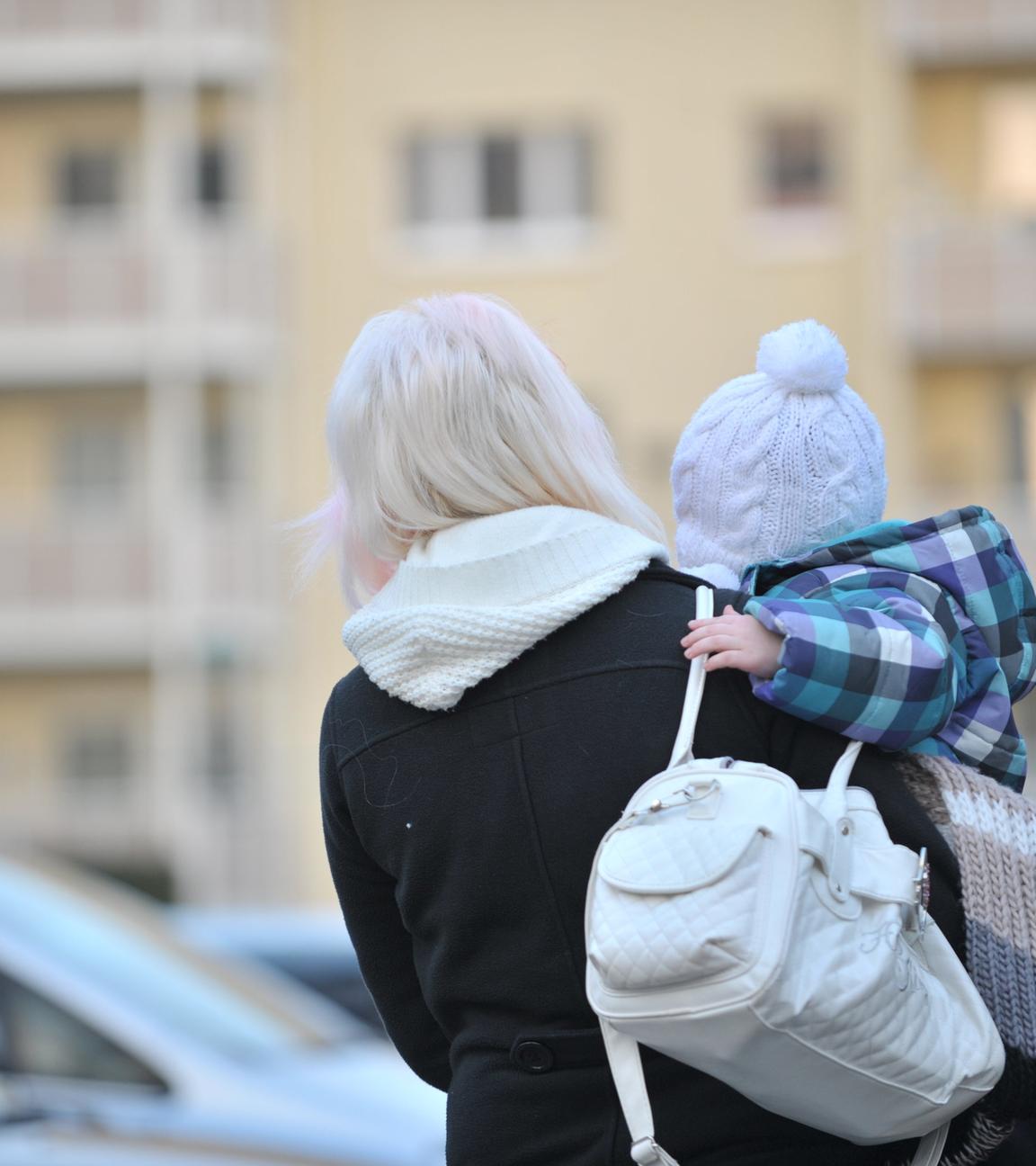 "Goldgrube Wohnungsnot – Spekulanten gegen Mieter": Mutter hält ihr kleines Kind auf dem Arm und schaut auf ein Wohnhaus.