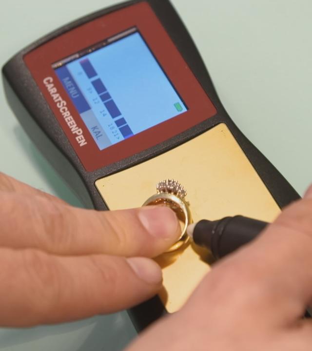 Person legt einen Goldring auf ein Messgerät und hält einen Stift an den Ring.