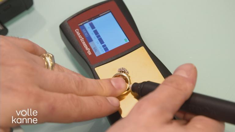 Person legt einen Goldring auf ein Messgerät und hält einen Stift an den Ring.