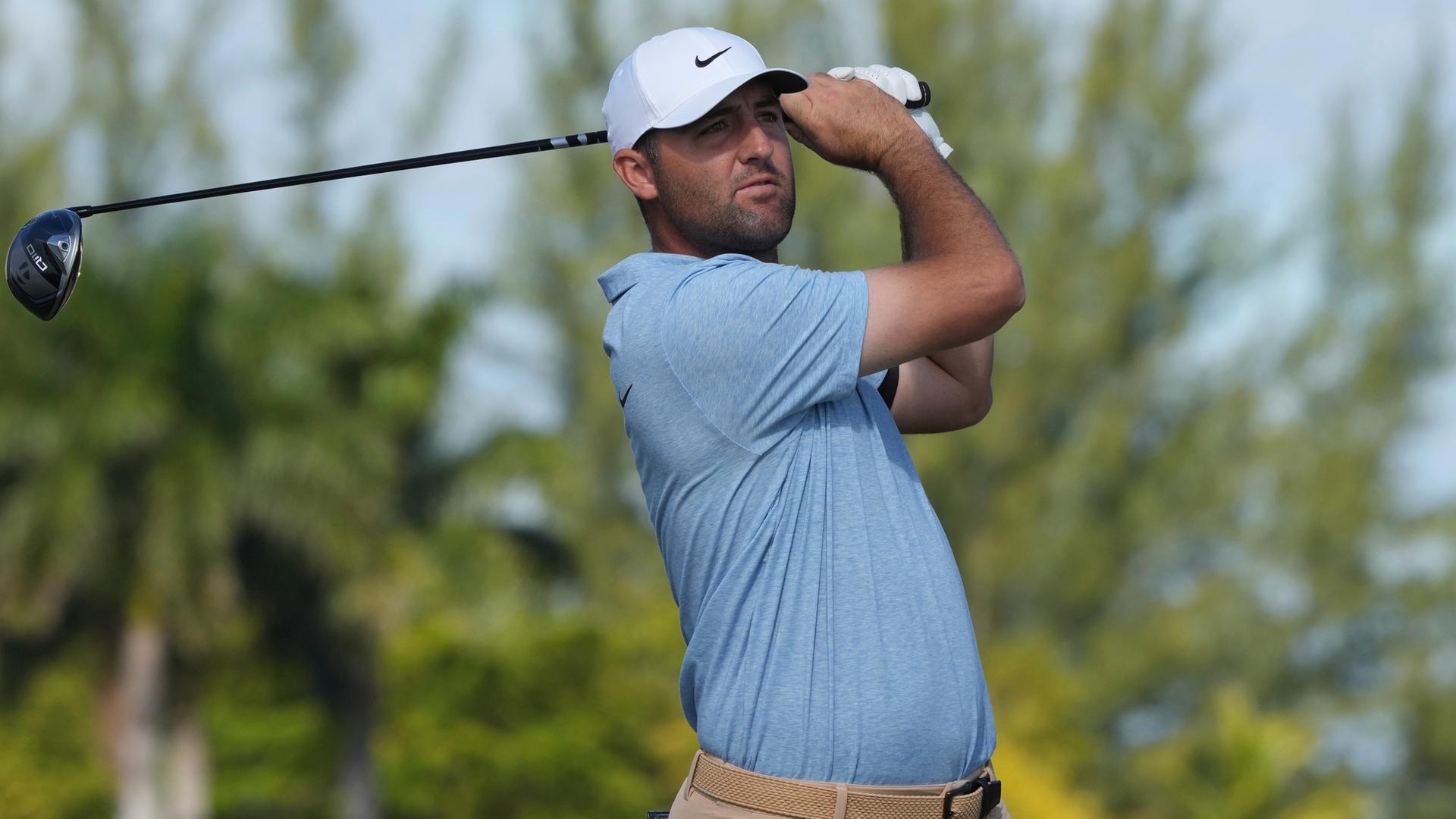 Der Golfer Scottie Scheffler nach seinem Schlag. Er schaut dem Ball nach und hält seinen Schläger hinter seinem Kopf.