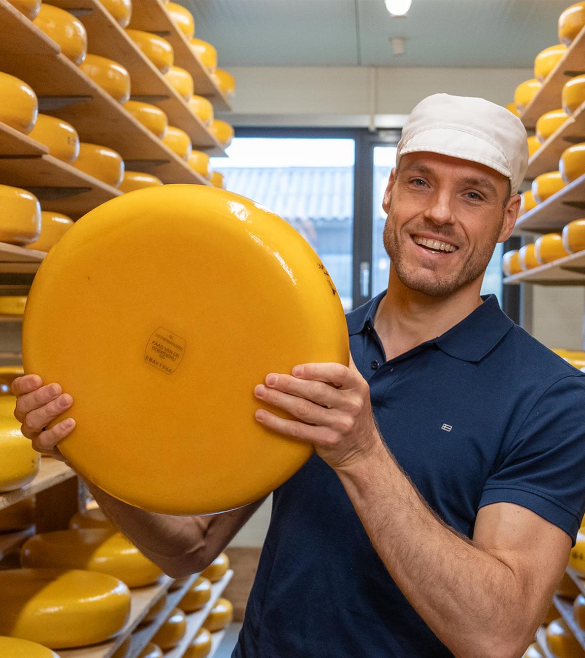 Mann hält großen Gouda-Käselaib in der Hand 