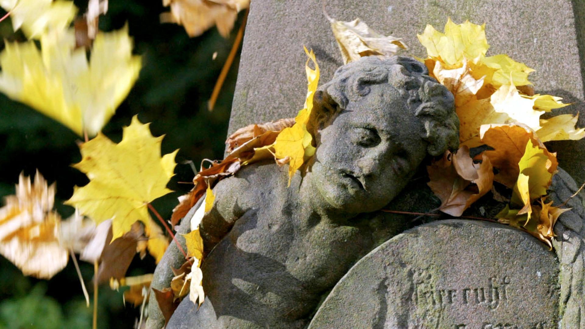 Symbolbild: Ein Grabstein mit Herbstlaub bedeckt.