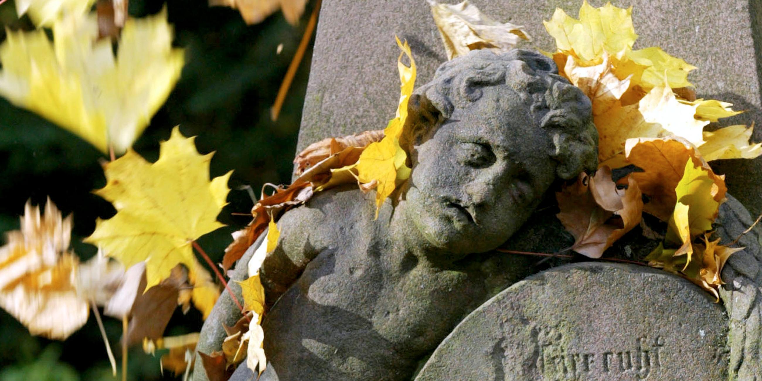 Symbolbild: Ein Grabstein mit Herbstlaub bedeckt.