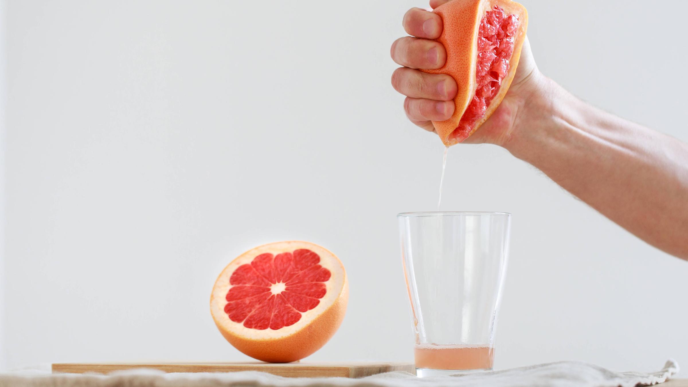 Mann presst halbe Grapefruit aus der Hand in ein Glas.
